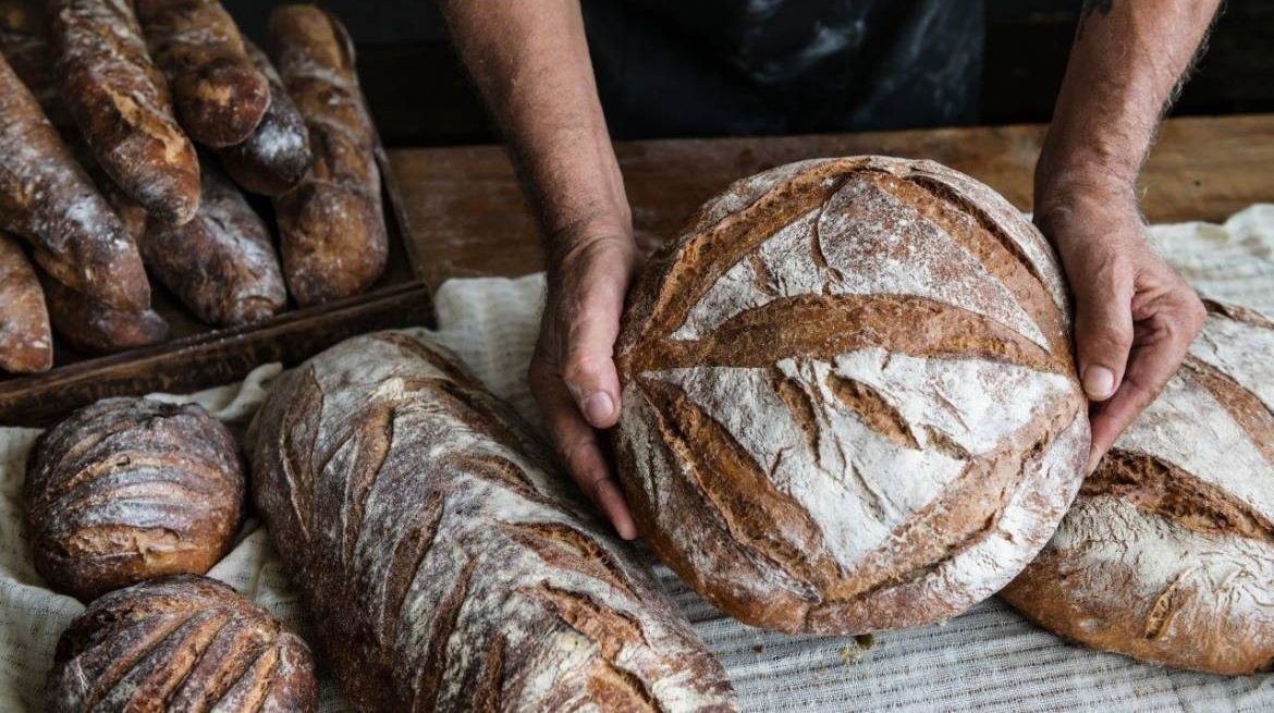 Des aliments simples, sains et nourrissants Pain frais avec croûte dorée, sur une table en bois, près de plusieurs autres pains.
